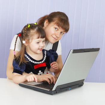 Mother and daughter playing with a computer at home sitting at the table