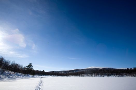 A ski trail going accross a frozen lake infront of a mountain landscape