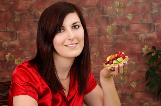 Young pretty woman holding a fruit tartlet