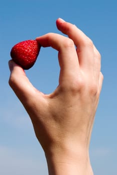 A hand holding a single strawberry against the sky