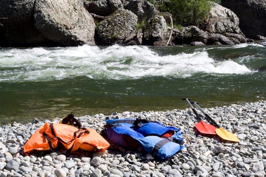 two  life-jackets and two paddles near river
