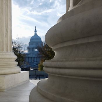 View of Capitol building in distance from behind columns of the Supreme Court building in Washington DC.