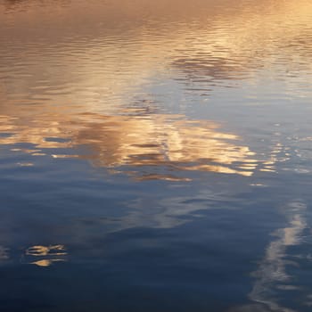 Reflections of orange and yellow sunset on rippling water.