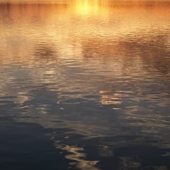 Reflections of orange and yellow sunset on water.