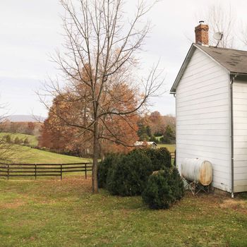 House in rural setting in Autumn with standing oil tank outside.