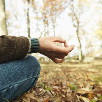 Caucasian man sitting on ground meditating in rural setting.