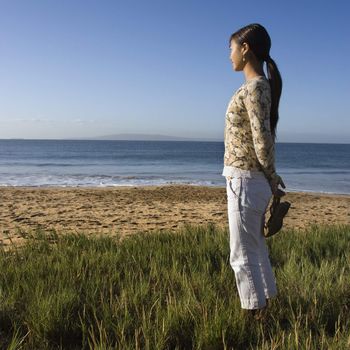 Young Asian female walking on beach and carrying her sandals.