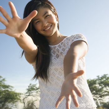 Young adult Asian female with arms and hands stretched out toward viewer.