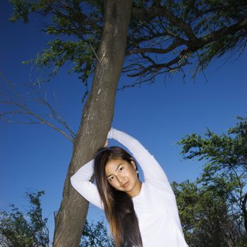 Young adult Asian female holding a tree and looking at viewer.