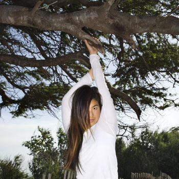 Young adult Asian female hanging from a tree looking at viewer.