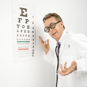 Mid-adult Caucasian male doctor wearing eyeglasses making gesture with eye chart in background.