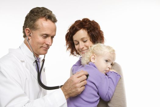 Middle-aged adult Caucasian male doctor holding stethoscope to female toddler's back with mother watching.