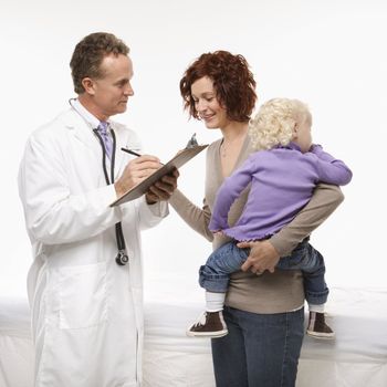 Middle-aged adult Caucasian male doctor taking notes on chart as mother holds daughter.