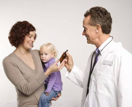 Middle-aged adult Caucasian male doctor handing Caucasian mother medication in a bottle.