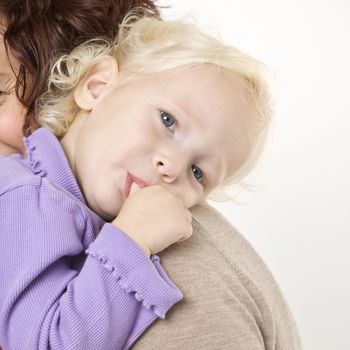 Caucasian female toddler sucking her thumb while her mother holds her.