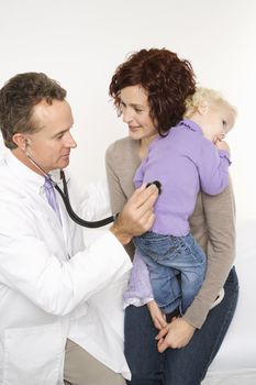 Caucasian mid-adult mother holding her female toddler while middle-aged male doctor uses stethoscope.