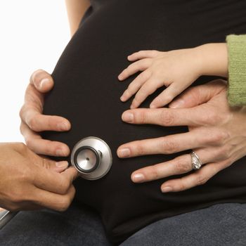 Nurse holding stethoscope to Caucasian pregnant woman's belly.