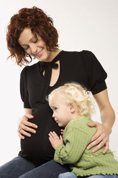 Young Caucasian female child with ear against her mother's pregnant belly.