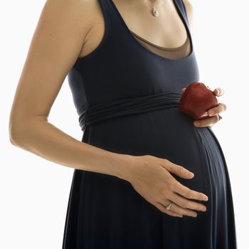 Portrait of Caucasion mid-adult pregnant woman with hands on belly holding an apple.