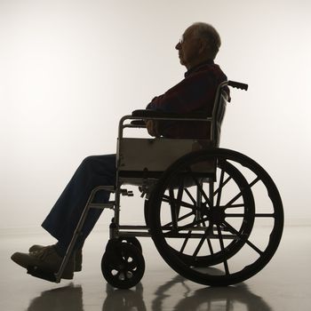 Profile view of silhouetted Caucasion elderly man sitting in wheelchair.