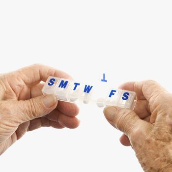 Caucasion elderly male hands holding seven-day pill box with Thursday open.