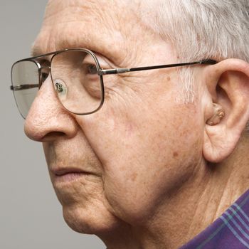 Close-up profile portrait of Caucasion elderly man with glasses and hearing aid.