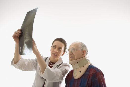 Mid-adult Caucasian female doctor showing x-ray to elderly Caucasian male in neck brace.