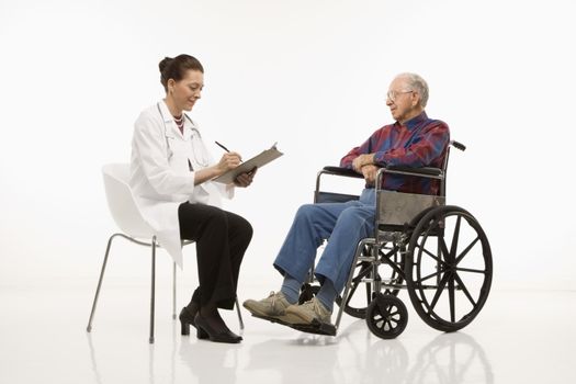 Mid-adult Caucasian female doctor taking notes with an elderly Caucasian male in wheelchair to her side.