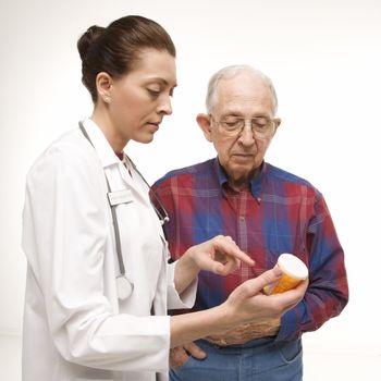 Mid-adult Caucasian female doctor pointing at prescription bottle as elderly Caucasian male looks at bottle.