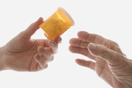 Close-up of mid-adult Caucasian female's hand handing medication bottle to elderly Caucasian male hand.