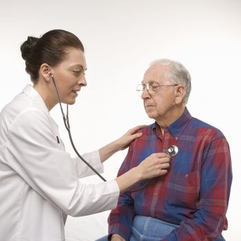 Mid-adult Caucasian female doctor listening to elderly Caucasian male's heartbeat with stethoscope.