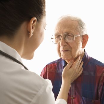 Mid-adult Caucasian female doctor checking an elderly Caucasian male's pulse.