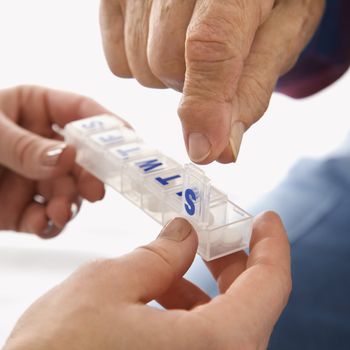 Mid-adult Caucasian female hands holding medication case for an elderly Caucasian male.