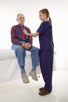Mid-adult Caucasian female in scrubs listening to elderly Caucasian male's heart beat.