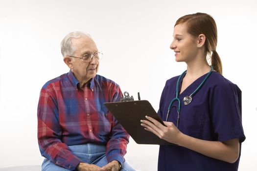 Mid-adult Caucasian female in scrubs taking notes from elderly Caucasian male.