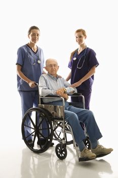 Two Caucasian females wearing scrubs with elderly Caucasian male in wheelchair.
