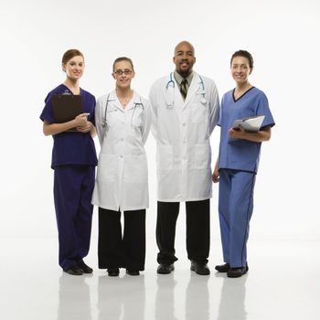 Full-length portrait of African-American man and Caucasian women medical healthcare workers smiling in uniforms standing against white background.