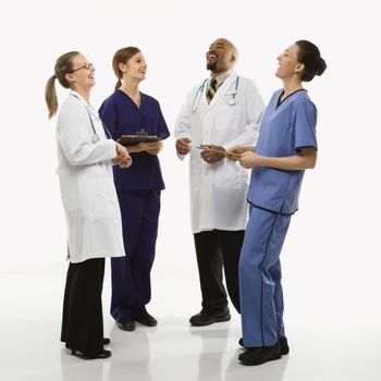 Full-length portrait of African-American man and Caucasian women medical healthcare workers in uniforms laughing standing against white background.