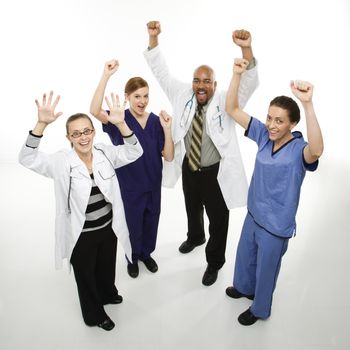 Full-length portrait of African-American man and Caucasian women medical healthcare workers in uniforms cheering with arms raised standing against white background.