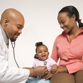 African-American male pediatrician examining baby girl being held by mother.