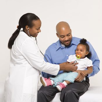 African-American female pediatrician examining baby girl being held by father.