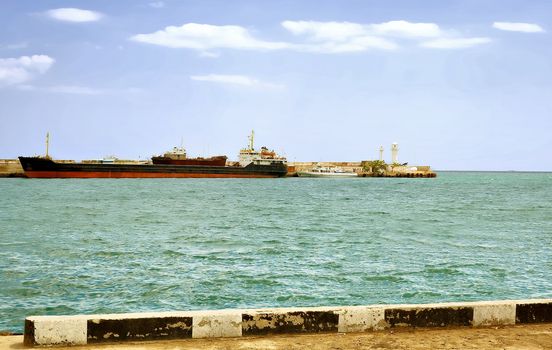 City Yalta. The peninsula of Crimea. Ukraine. Sunny day transport ship is far from the pier. Adjacent to the small boat. Even farther on the edge of the pier stands a lighthouse.