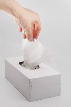 female hand pulling white facial tissue from a box