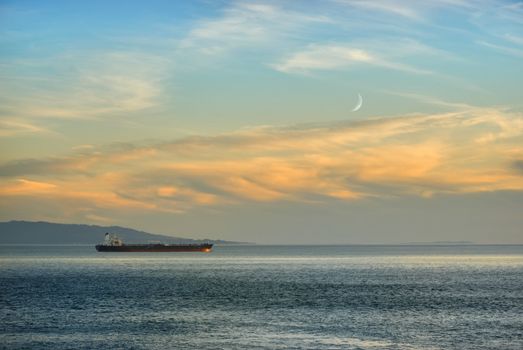 Ship in twilight on the ocean with new moon in background.