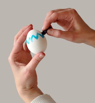 Female hands coloring an easter egg with gray background that is easy to remove