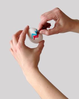 Female hands coloring an easter egg with gray background that is easy to remove