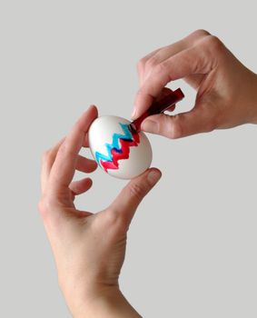 Female hands coloring an easter egg with gray background that is easy to remove