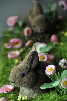 Easter decoration with rabbits, eggs and daisies on faked grass..