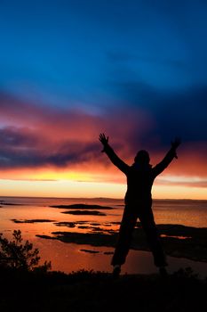 A person standing by the ocean raising their arms in celebration