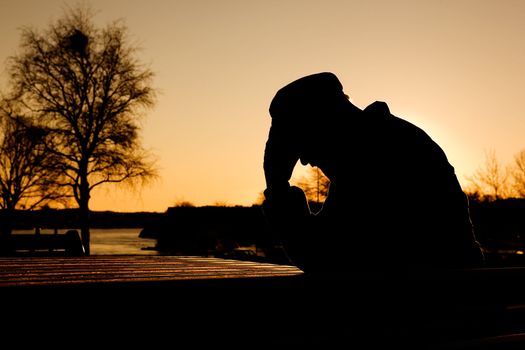 A depressed thoughtful man by the water at sundown